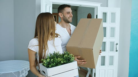 Couple carrying moving box and plant.
