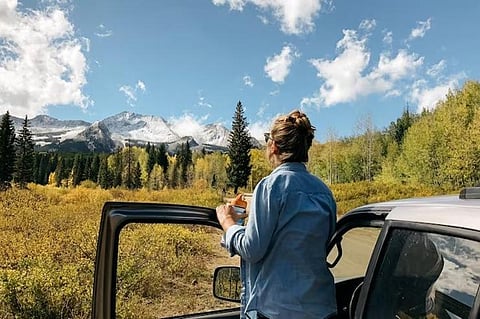 Woman by car looking at mountains.