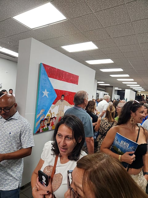A crowded gallery at I Am Art PR with a painted Puerto Rican flag work on the wall