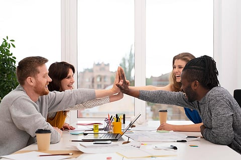 Coworkers high-fiving across a desk.