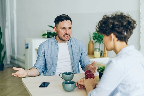 Man gesturing while talking to a woman at a table.