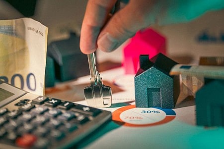 Hand holding a key above model houses and a calculator.