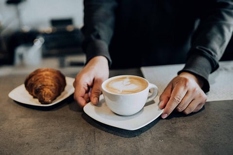 Hands holding coffee and a croissant.