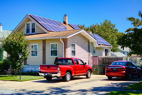 House with rooftop solar panels and two red vehicles.