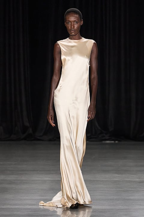Model in an ivory satin gown on a dark runway