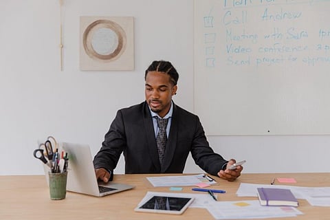 Businessman using laptop and phone at desk.