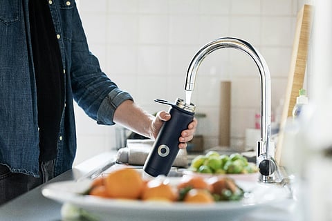 Person filling a water bottle at a kitchen faucet.