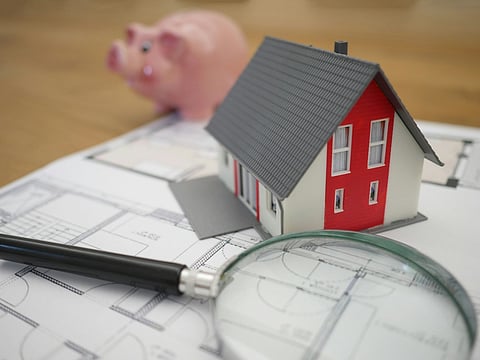 Model house, piggy bank, and magnifying glass on blueprints.