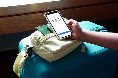 Hand holding phone over passport and suitcase.