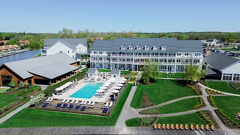 Aerial view of lakefront hotel with a rectangular pool, lawns and a lake in the distance