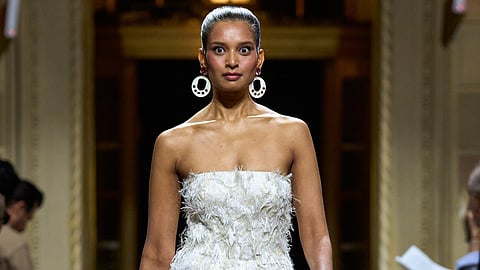 Model in a strapless white gown covered in fluttering white feathers walking a marble runway