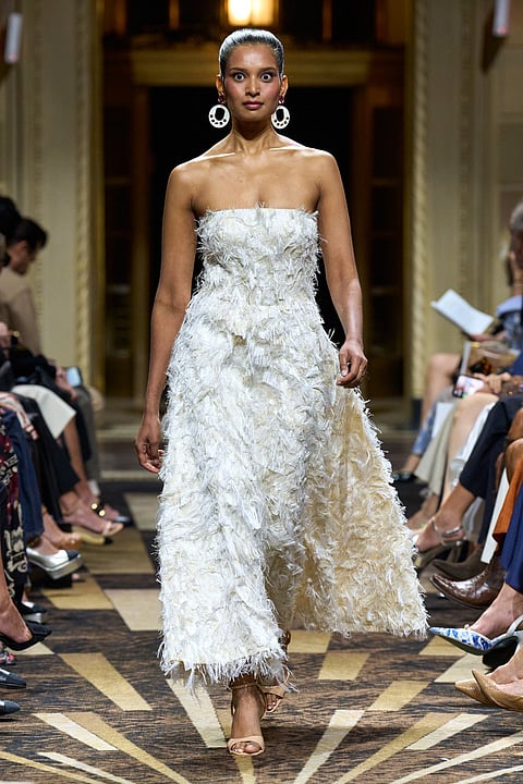 Model in a strapless white gown covered in fluttering white feathers walking a marble runway
