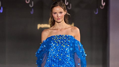 Model in an off-the-shoulder cobalt blue gown covered in layered feather-like paillettes on a runway