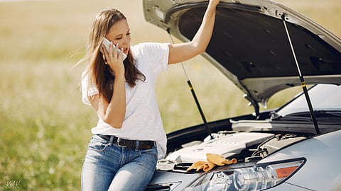 Woman on phone by car with open hood.