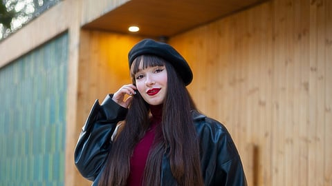 Woman in a black beret and leather jacket posing outdoors.