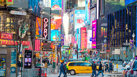 Billboards, theater signs, and a yellow taxi on a busy Times Square street