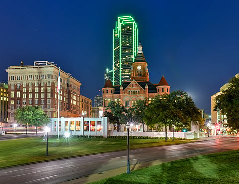 Old Red Museum's red stone courthouse at dusk, with a green-lit tower behind it in Dallas