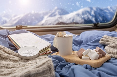 Coffee, map, and compass on a bed with a snowy mountain view.