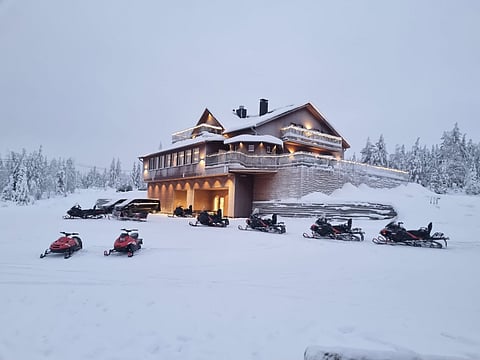Otava Lodge, a three-story timber lodge on a snowy hilltop in Finnish Lapland, with snowmobiles