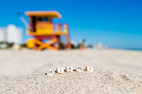 Letter beads spelling MIAMI in the sand in front of a yellow lifeguard tower on South Beach