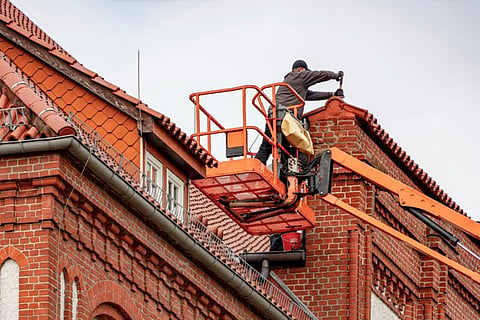 Worker in a cherry picker repairing a brick building.