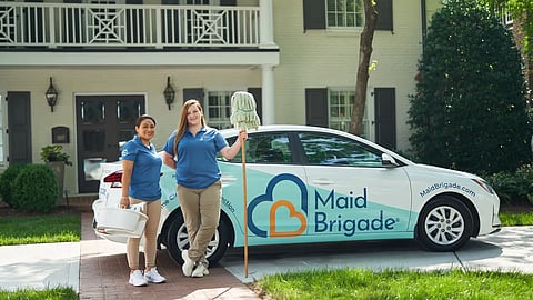 Two cleaners standing by a Maid Brigade car.