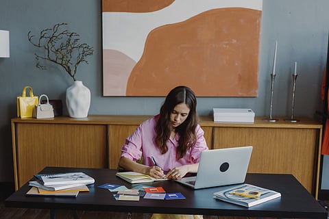 Woman writing at a desk with a laptop.