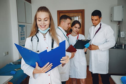 oung doctor reading a medical folder with colleagues in the background.