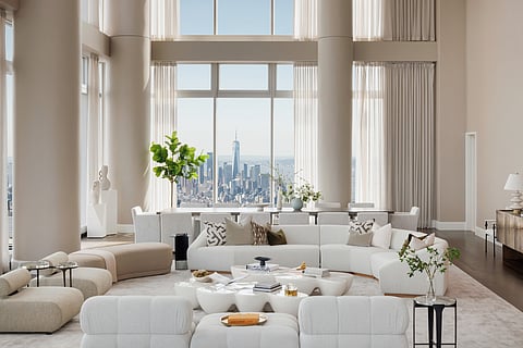 Double-height penthouse living room with massive beige columns, curved boucle sofas