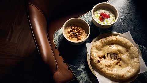 Torn sourdough pita beside bowls of whipped dips on a table at Naia in Fort Lauderdale