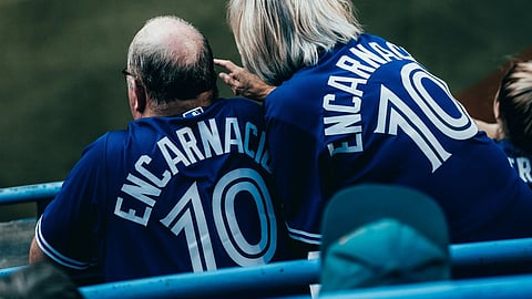 Two fans wearing matching blue baseball jerseys in the stands overlooking a field.