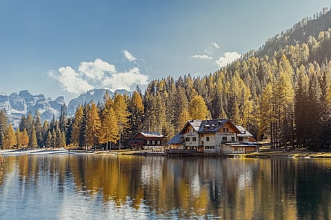 Lakeside house surrounded by autumn trees and mountains.