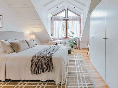 Bright attic bedroom with a bed and white wardrobes.