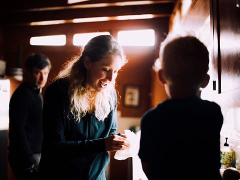 Elizabeth Holmes smiling in a dim kitchen while Nathan Fielder looks on in the background
