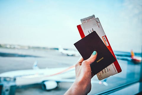 Hand holding a passport and boarding pass at an airport window.