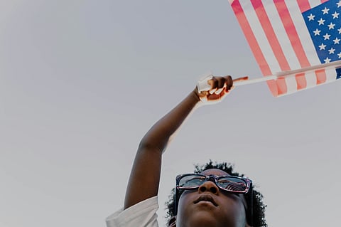 Child holding an American flag against the sky.