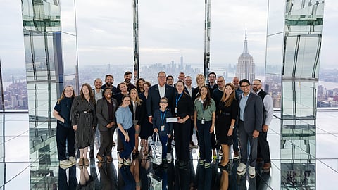 Group posing in a mirrored glass room with the Manhattan skyline and Empire State Building behind