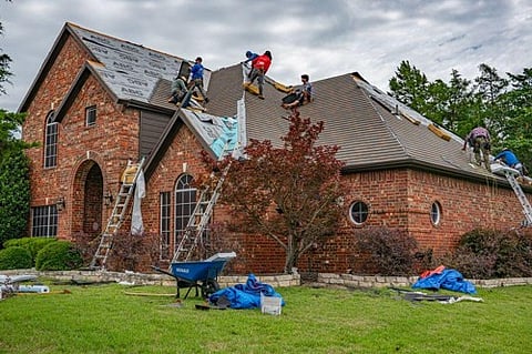 Roofers installing shingles on a brick house.