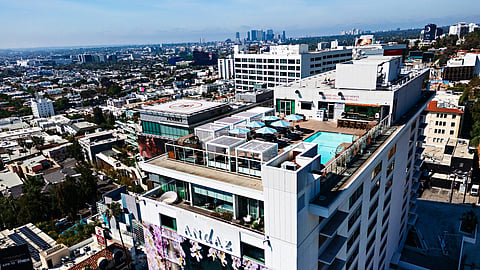 Aerial view of a hotel tower with a rooftop pool and the Los Angeles skyline beyond