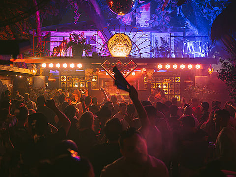 Crowd with raised arms under a wooden canopy lit in pink and blue