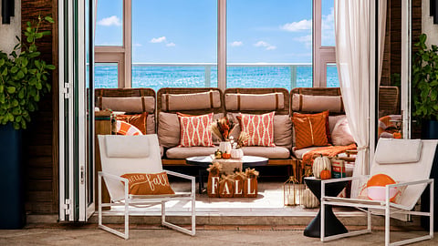 Guests on a poolside cabana lounger with orange cushions, pumpkins and a bay view