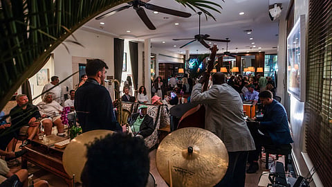 A trio with upright bass, saxophone and drums performs beside a grand piano in a lounge