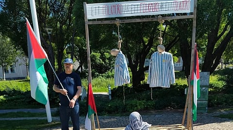 Den tidigare S-politikern Mahmoud Shnino poserar med en palestinaflagga framför de hängda förintelsedockorna i Vänortsparken i centrala Umeå. Han hördes inte i utredningen.