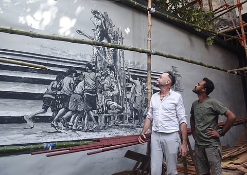 हातीबागान सार्वजनिन के पूजा पंडाल में अपनी पेंटिंग की ओर देखते थॉमस हेनरिओट और तापस दत्ता 