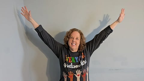 Sheila Applegate with hands in air wearing an Everyone Is Welcome Tshirt 