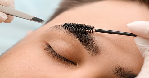 A close-up of a stylist working on the eyebrows of a client. They are using a brush and tweezers to get them perfect.