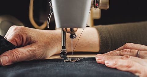 A woman's hand pushing a piece of fabric through the needle of a sewing machine. The fabric is a dark blue color.