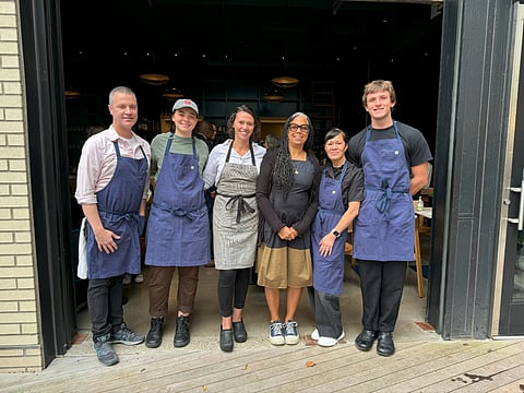 The staff at Marjorie. Donna Moodie is third from right. The staff members are standing at the entrance with their arms around one another and smiling for the photo.