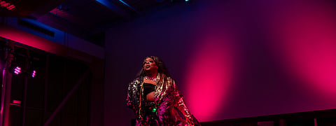 Seattle drag queen Londyn Bradshaw performs "Mt. Everest" by Labyrinth in front of the audience at the ninth annual Legendary Children event. She is wearing sparkly clothing and cast in colorful lighting.