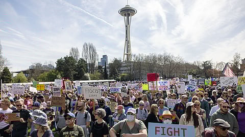 Large crowd gathered at a protest in Seattle's Seattle Center, with the Space Needle visible in the background. People hold diverse signs with messages like “FIGHT OLIGARCHY,” “SAVE OUR STUDENTS,” and “NO FASCIST LIARS,” reflecting a strong call for democracy and justice.